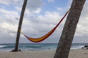 Waves roll in toward the shore of Lighthouse Caye off the coast of Belize as a hammock hangs between two palm trees.
